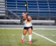 Field hockey player in action, striking a ball on a lit field, showcasing athleticism and focus during a nighttime game.