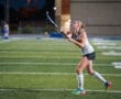 Field hockey player practicing at night on an artificial turf field, focused on hitting the ball with a stick.