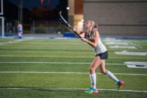 Field hockey player practicing at night on an artificial turf field, focused on hitting the ball with a stick.