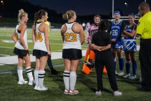 Field hockey players gather for a pre-game meeting under stadium lights, showcasing teamwork and sportsmanship.