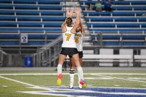 Two female soccer players jump in celebration on the field, wearing uniforms with the numbers 7 and 4.