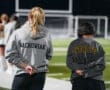 Two soccer players in sweatshirts stand on the field, focused and waiting for a game to begin under stadium lights.