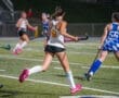 High school girls playing field hockey under stadium lights, showcasing teamwork and athleticism during a night match.