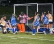 Field hockey players compete fiercely under the lights, with a goalie ready to defend the goal in a thrilling match.