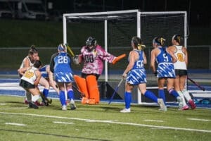Field hockey players compete fiercely under the lights, with a goalie ready to defend the goal in a thrilling match.
