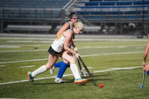 Two field hockey players compete on a turf field, focusing on a red ball while showcasing athletic skill and teamwork.