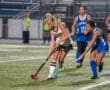 High school field hockey players compete for the ball during an exciting night match on a lit field.