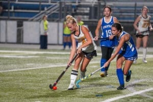 High school field hockey players compete for the ball during an exciting night match on a lit field.