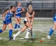 Two field hockey players compete for the ball under stadium lights, showcasing athleticism and teamwork in action.
