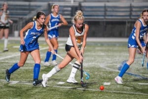 Two field hockey players compete for the ball under stadium lights, showcasing athleticism and teamwork in action.