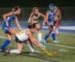 High school field hockey players compete under stadium lights, with one player skillfully controlling the ball on the field.