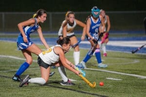 High school field hockey players compete under stadium lights, with one player skillfully controlling the ball on the field.