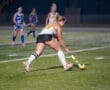 Young female field hockey player dribbling the ball on an illuminated field during a nighttime match.
