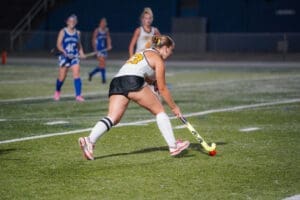 Young female field hockey player dribbling the ball on an illuminated field during a nighttime match.