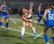 High school field hockey players compete under stadium lights, showcasing dynamic action and athleticism on the field.
