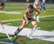Field hockey players compete for the ball during a night match, showcasing teamwork and athleticism on the turf.