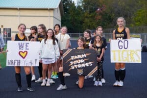 Cheerleaders and youth supporters holding signs at a sports event, promoting positivity and team spirit for the Tigers.