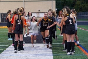 Team celebration as players run through a spirit line of teammates, showcasing joy and camaraderie at a field hockey event.