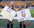 Two young fans cheer at a sports event, holding signs that say Go Tigers and We ♥ Math Youth! on the field.