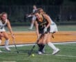 High school girls' field hockey players competing for the ball on the turf during an evening match.