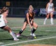Field hockey players compete for the ball under stadium lights, showcasing athleticism on the turf during a match.