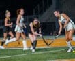 High school girls' field hockey game action with players in uniforms competing on the field under stadium lights.
