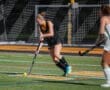 A field hockey player dribbles the ball on a night-lit turf, showcasing athletic skills during a competitive match.