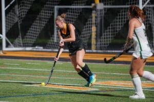 A field hockey player dribbles the ball on a night-lit turf, showcasing athletic skills during a competitive match.