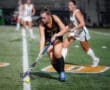 Field hockey players in action, one dribbling a yellow ball while another defender pursues during a night game.