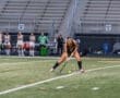 Player in a black jersey prepares to hit a ball during a field hockey match, with teammates in the background.