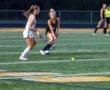 Two field hockey players engage in a competitive match on a turf field, focusing on the ball.