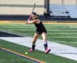 A field hockey player in action, striking a ball on a vibrant turf field during practice.