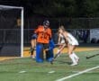 Field hockey players in action at night, featuring a goalie blocking a shot in an intense game.