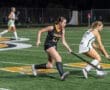 Field hockey players compete for the ball on a vibrant turf field during an intense night game.