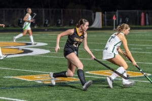 Field hockey players compete for the ball on a vibrant turf field during an intense night game.