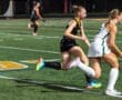 Two field hockey players sprinting on the turf during a competitive match, showcasing speed and teamwork.
