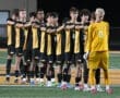 High school soccer team standing in a row, arms crossed, showing team spirit before a match. Goalkeeper in yellow.