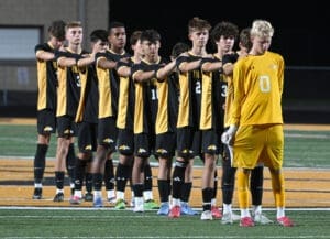 High school soccer team standing in a row, arms crossed, showing team spirit before a match. Goalkeeper in yellow.