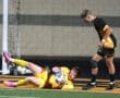 A goalkeeper makes a save while a teammate watches during a night soccer match on a turf field.