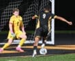 Soccer players in action: a forward dribbles past the goalkeeper during a night game. Excitement unfolds on the field.