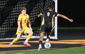Soccer players in action: a forward dribbles past the goalkeeper during a night game. Excitement unfolds on the field.
