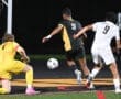 Soccer players compete for the ball near the goal during a night match, showcasing athleticism and teamwork.