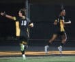 Two soccer players celebrate a goal on the field at night, showcasing team spirit and excitement in their victory.