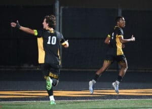 Two soccer players celebrate a goal on the field at night, showcasing team spirit and excitement in their victory.