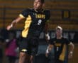 Player from the Tigers soccer team jumps to head the ball during a night game, showcasing athleticism and teamwork.