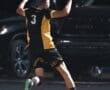 Soccer player in black and yellow jersey celebrates a goal with excitement under the stadium lights.