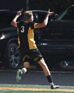 Soccer player in black and yellow jersey celebrates a goal with excitement under the stadium lights.