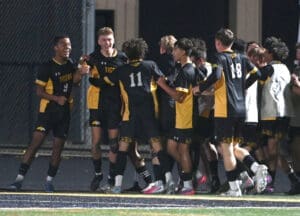 High school soccer team celebrating a goal under stadium lights, showcasing teamwork and excitement on the field.