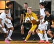 High school soccer match with players clustered around the goal, goalkeeper in yellow preparing to catch the ball.