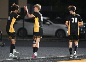 Three soccer players celebrate on the field, showcasing team spirit and camaraderie during a nighttime match.